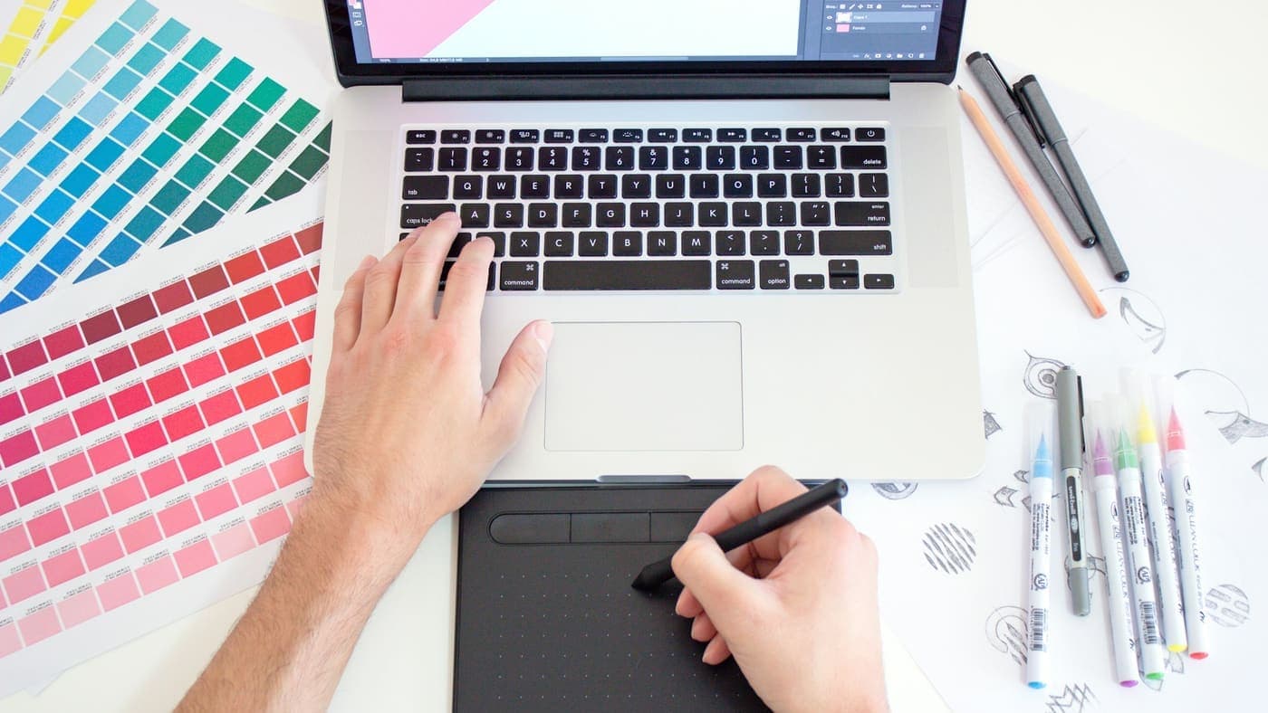 Designer travaillant sur une mise en page, nuancier de couleurs à côté de son ordinateur
